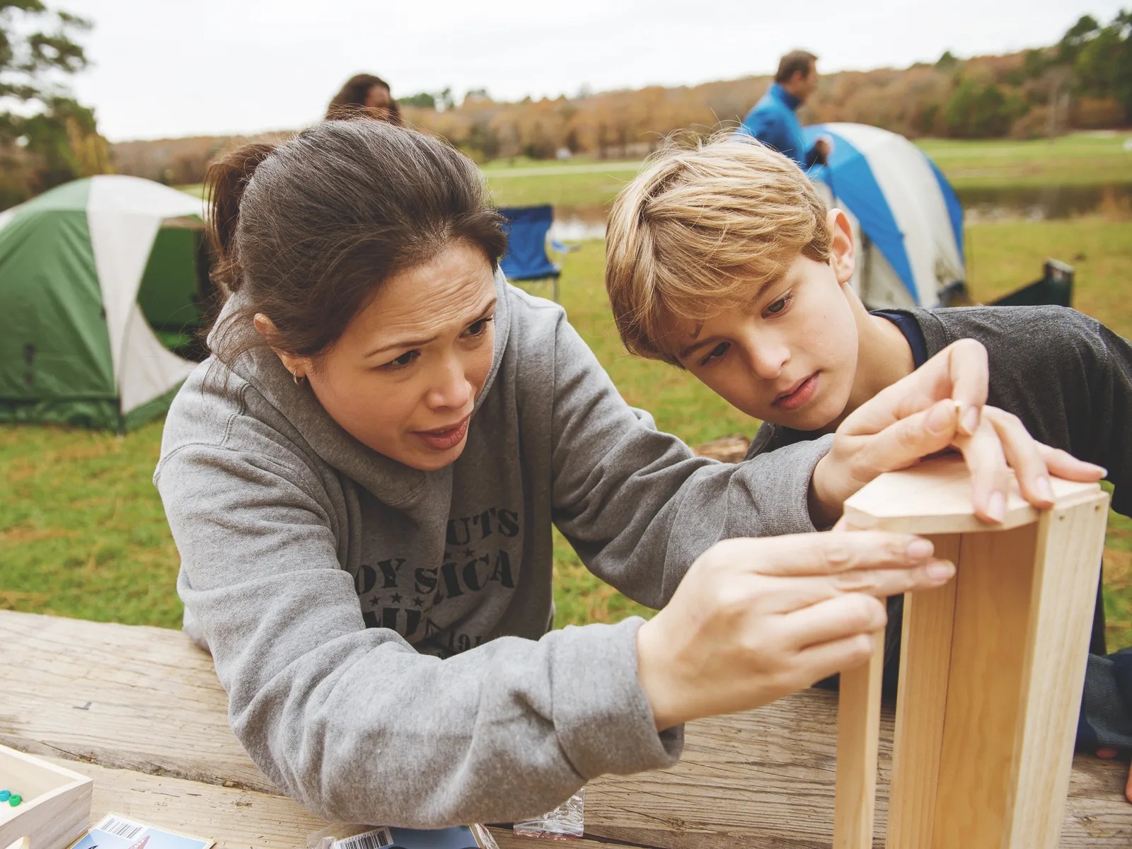 A parent and a Cub Scout building a birdhouse together at a campsite