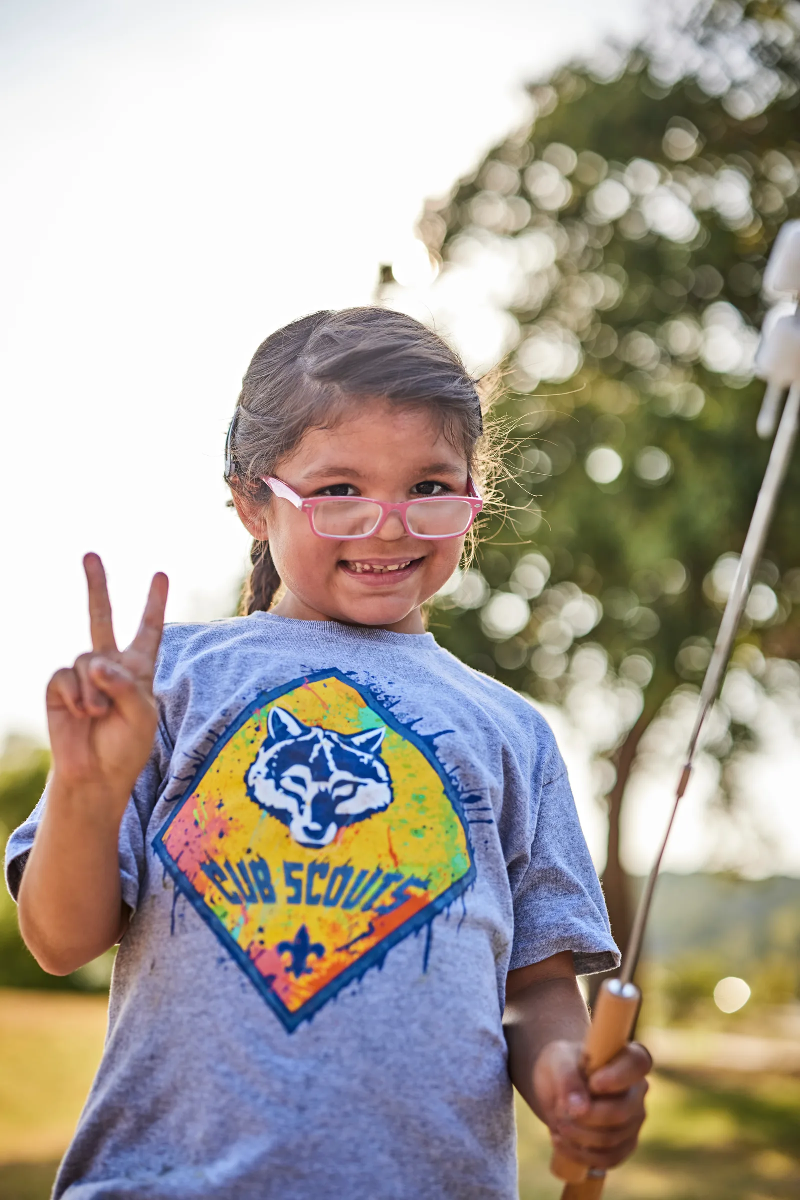 A young Cub Scout in a pack t-shirt holding a fishing rod and making a peace sign