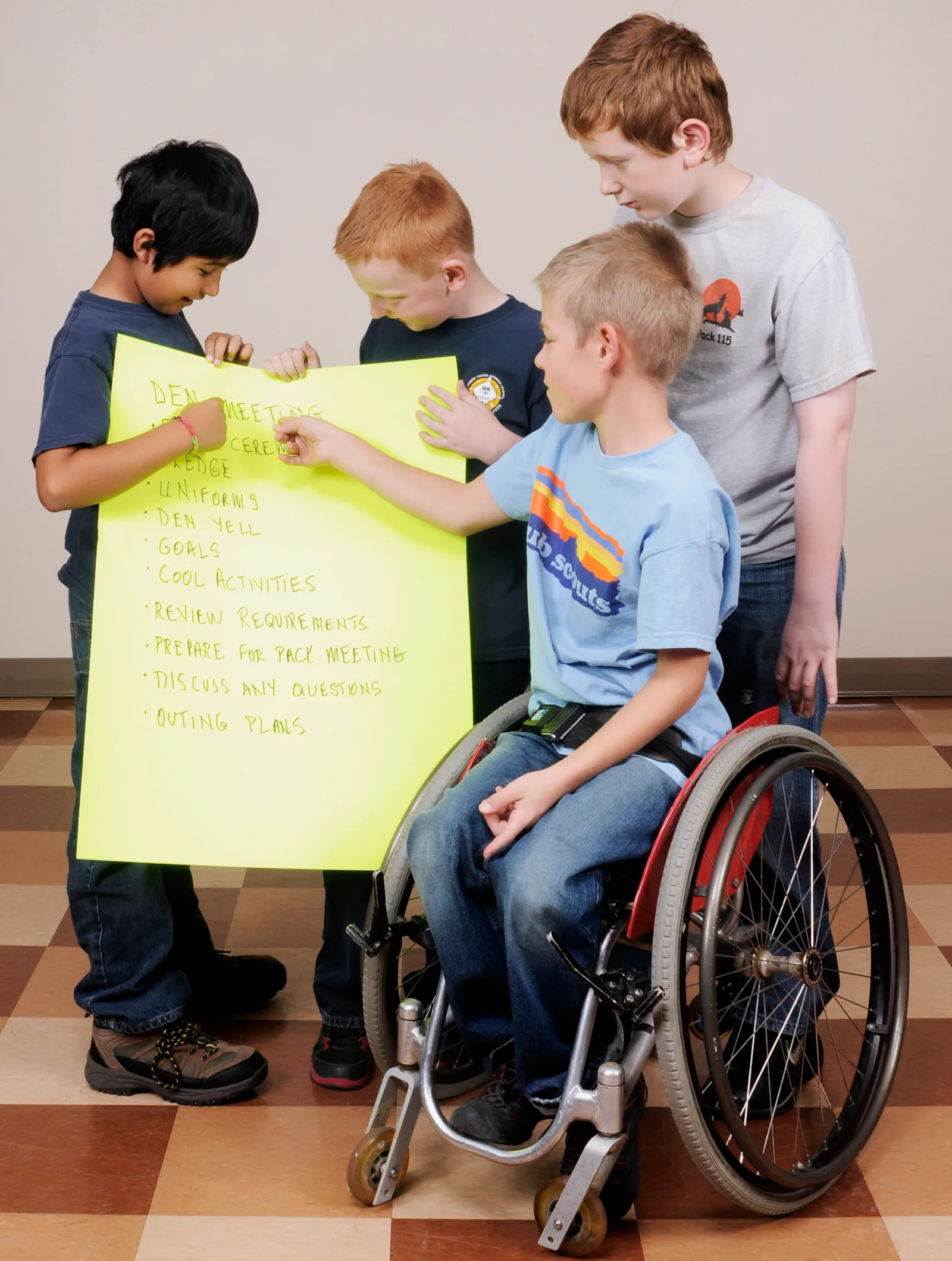 Cub Scouts working together on a poster, one of them using a wheelchair