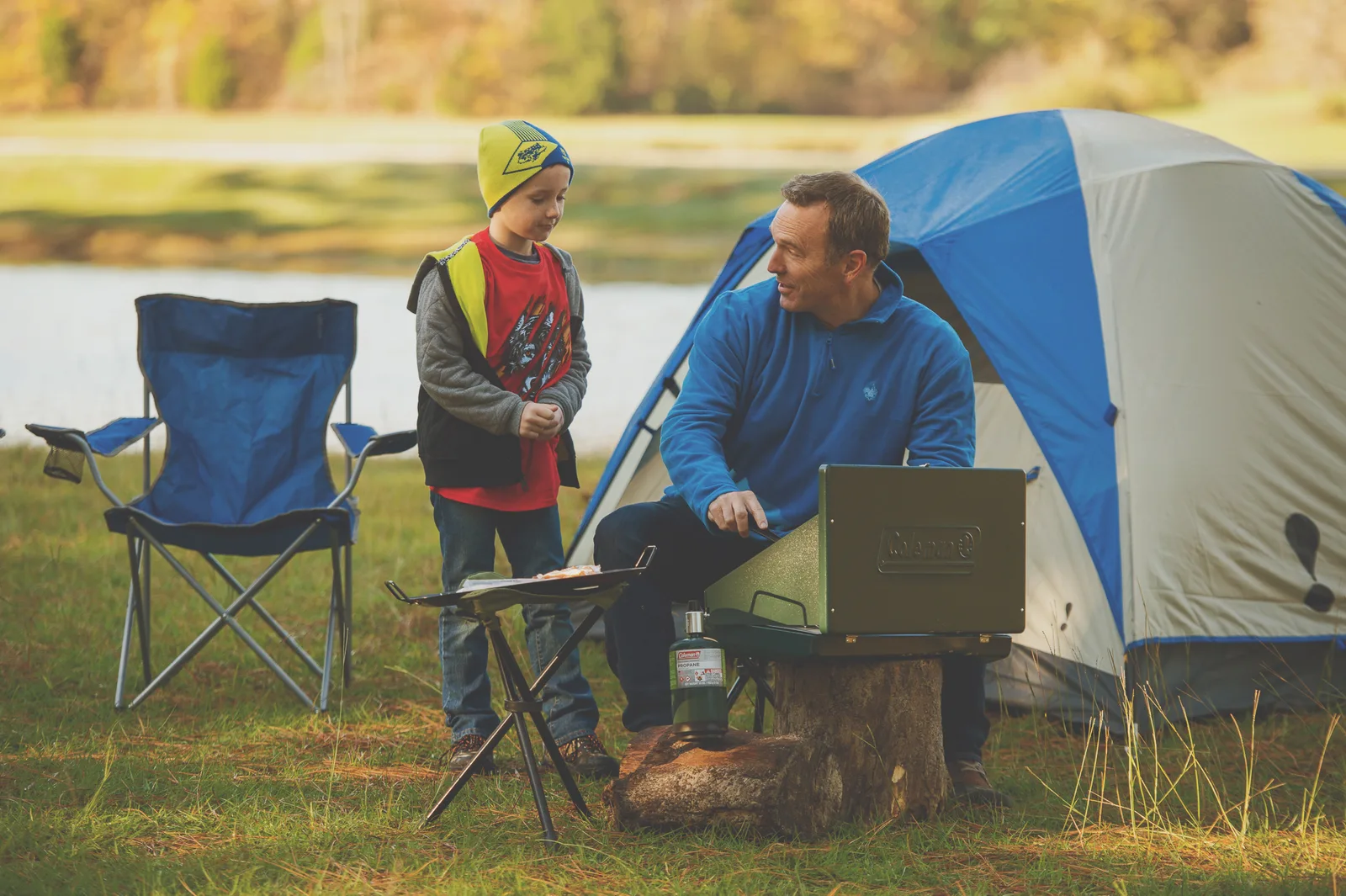A parent and child at their campsite beside a tent, cooking on a camp stove