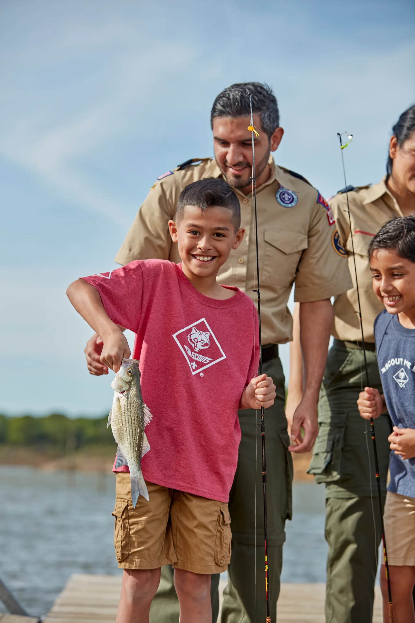 A Cub Scout holding up a fish he caught while leaders and other Scouts look on