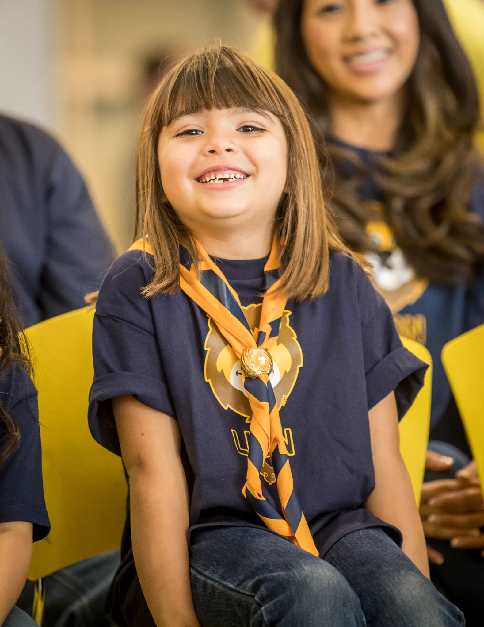 A Cub Scout in uniform and neckerchief laughing during a pack meeting