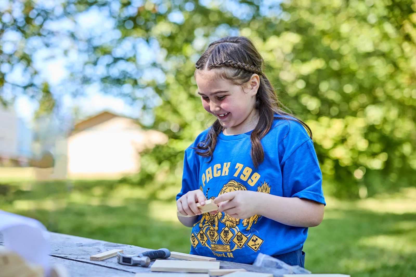 A Cub Scout sanding a block of pine into a Pinewood Derby car at a picnic table