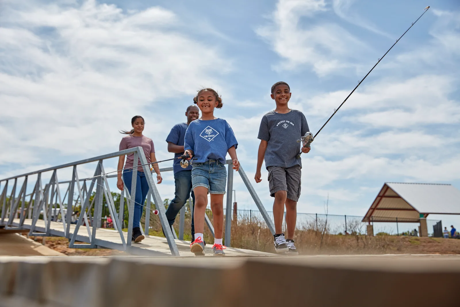 Cub Scouts walking across a wooden footbridge carrying fishing rods