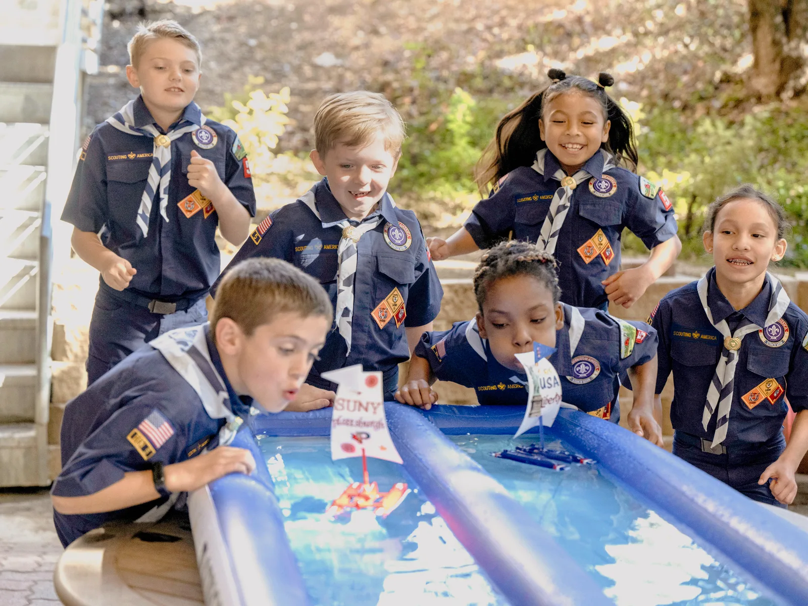 Cub Scouts blowing model sailboats down a water-filled rain gutter