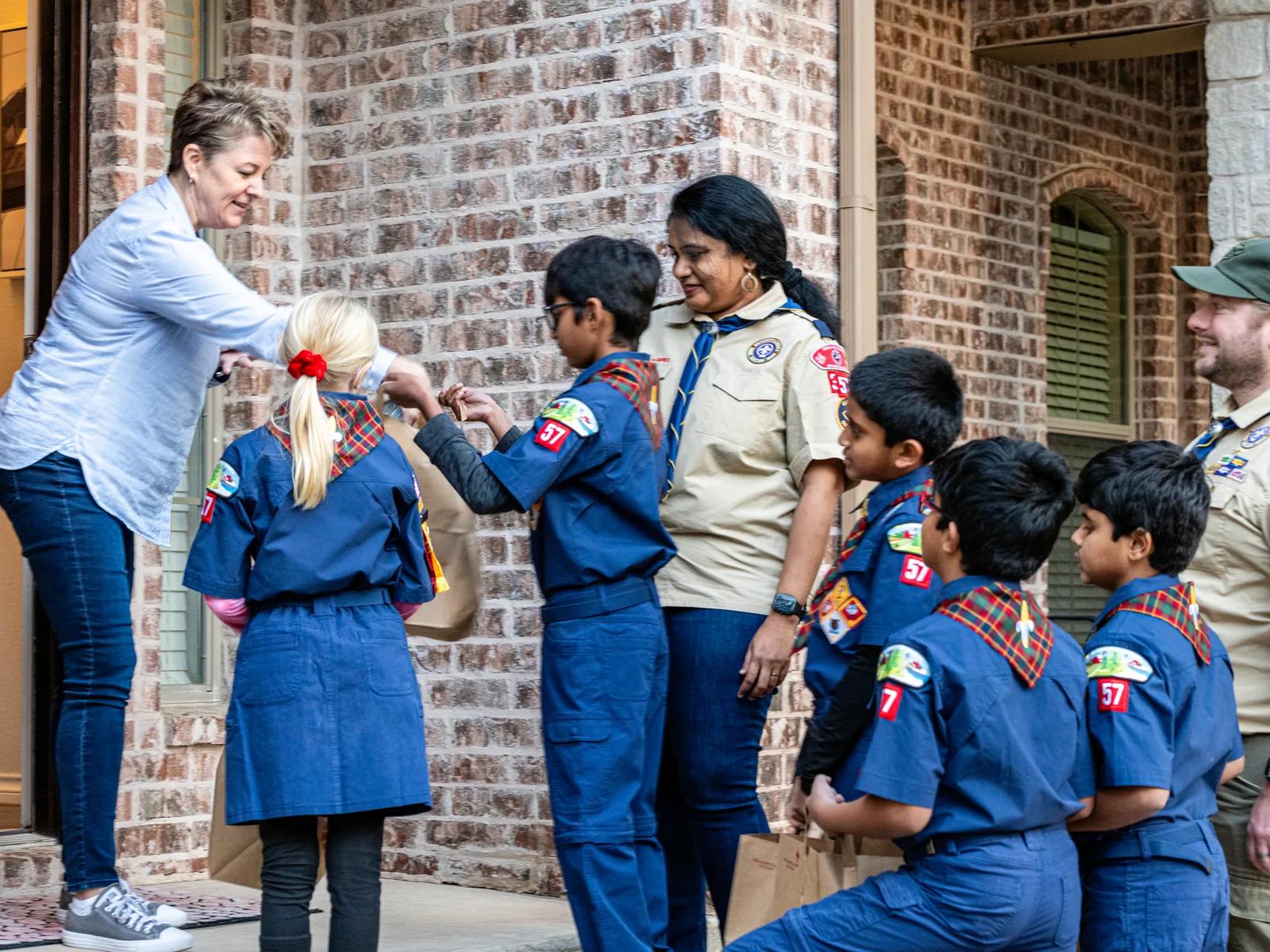Cub Scouts and adult leaders collecting food donations at a doorstep